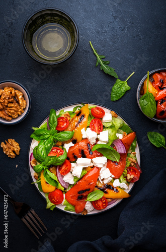 Fresh healthy salad with grilled paprika, feta cheese, walnut, red onion, green basil and mixed herbs, black table background, top view