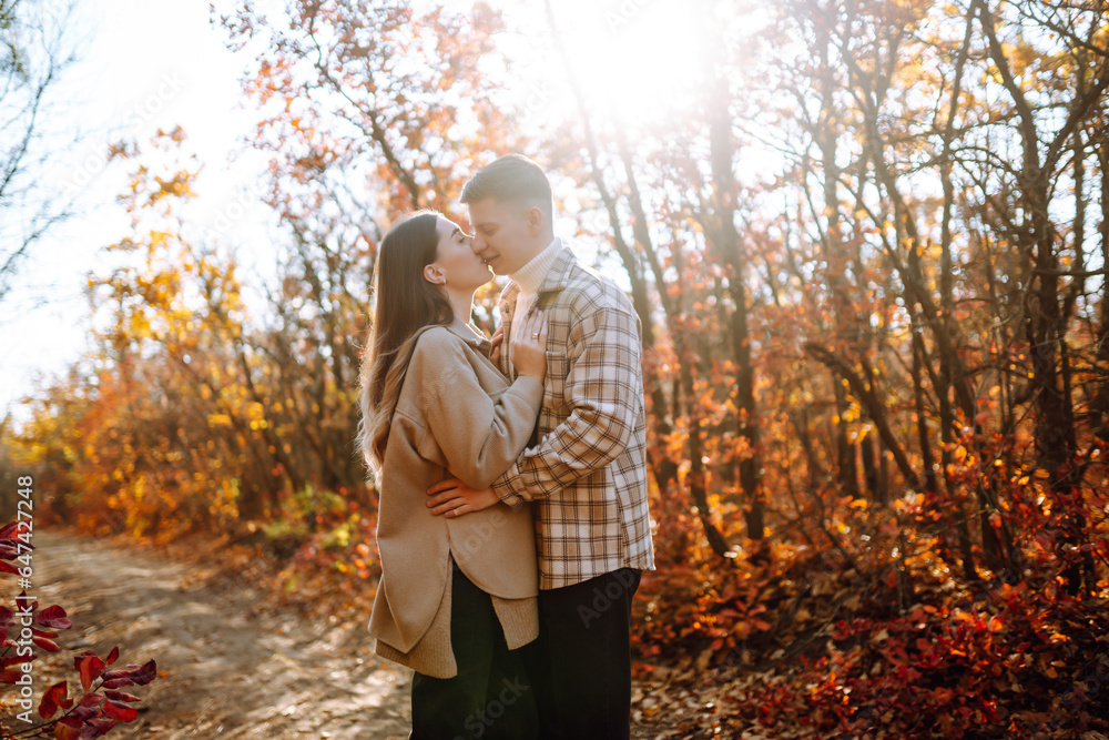 Young man and woman are walking, spending time together in the autumn forest. Beautiful couple enjoying nature outdoors in autumn. Concept for style, fashion, love or relaxation.