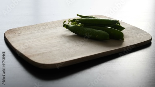 Garden pea (Pisum sativum) pods on a wooden chopping board, in a pile. Landscape orientation, view from the side. photo