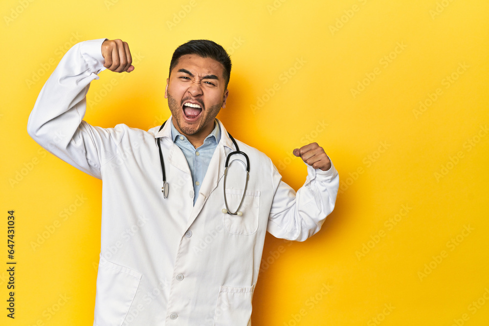 Asian doctor in white coat with stethoscope, yellow studio raising fist after a victory, winner concept. Asian doctor in white coat with stethoscope, yellow studio raising fist after a victory, winner concept.