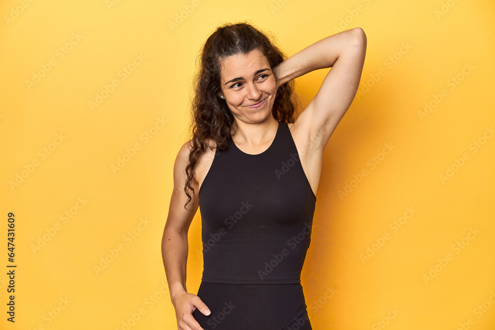 Sporty woman in active wear, yellow backdrop, touching back of head, thinking and making a choice. Sporty woman in active wear, yellow backdrop, touching back of head, thinking and making a choice.
