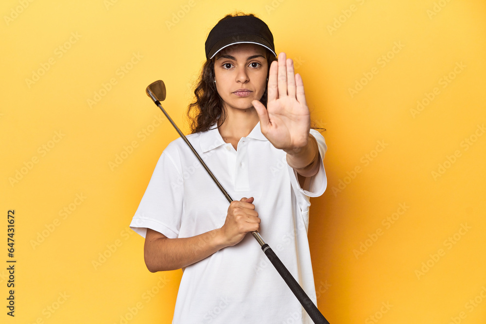 Golfer woman with cap, golf polo, yellow studio, standing with outstretched hand showing stop sign, preventing you. Golfer woman with cap, golf polo, yellow studio, standing with outstretched hand showing stop sign, preventing you.