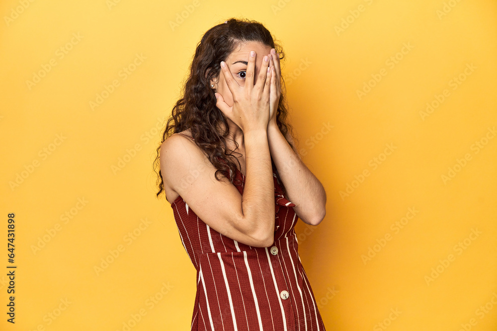 Young Caucasian woman, yellow studio background, blink through fingers frightened and nervous. Young Caucasian woman, yellow studio background, blink through fingers frightened and nervous.