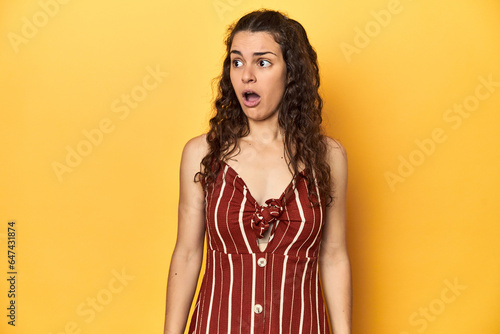 Young Caucasian woman, yellow studio background, being shocked because of something she has seen.