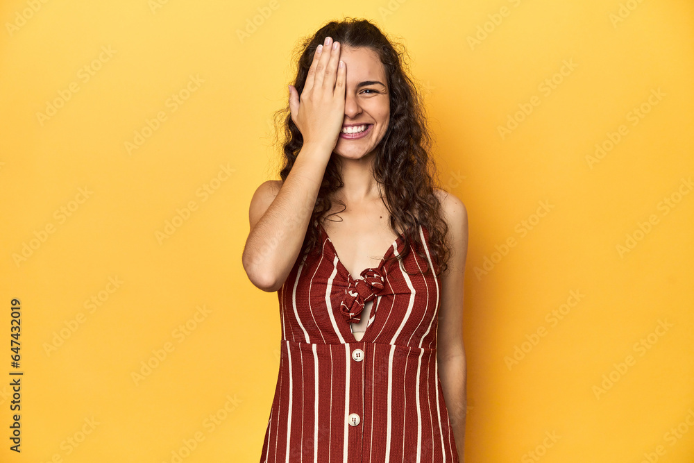 Young Caucasian woman, yellow studio background, having fun covering half of face with palm. Young Caucasian woman, yellow studio background, having fun covering half of face with palm.