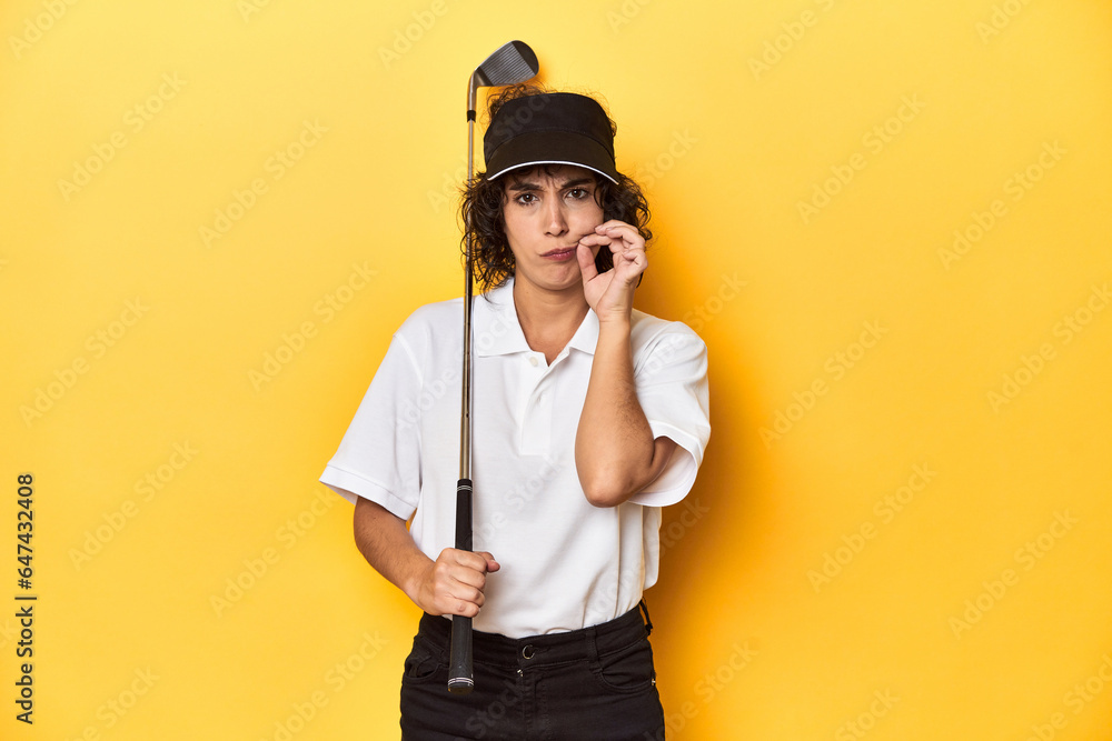 Athletic Caucasian woman with curly hair golfing in studio with fingers on lips keeping a secret.
