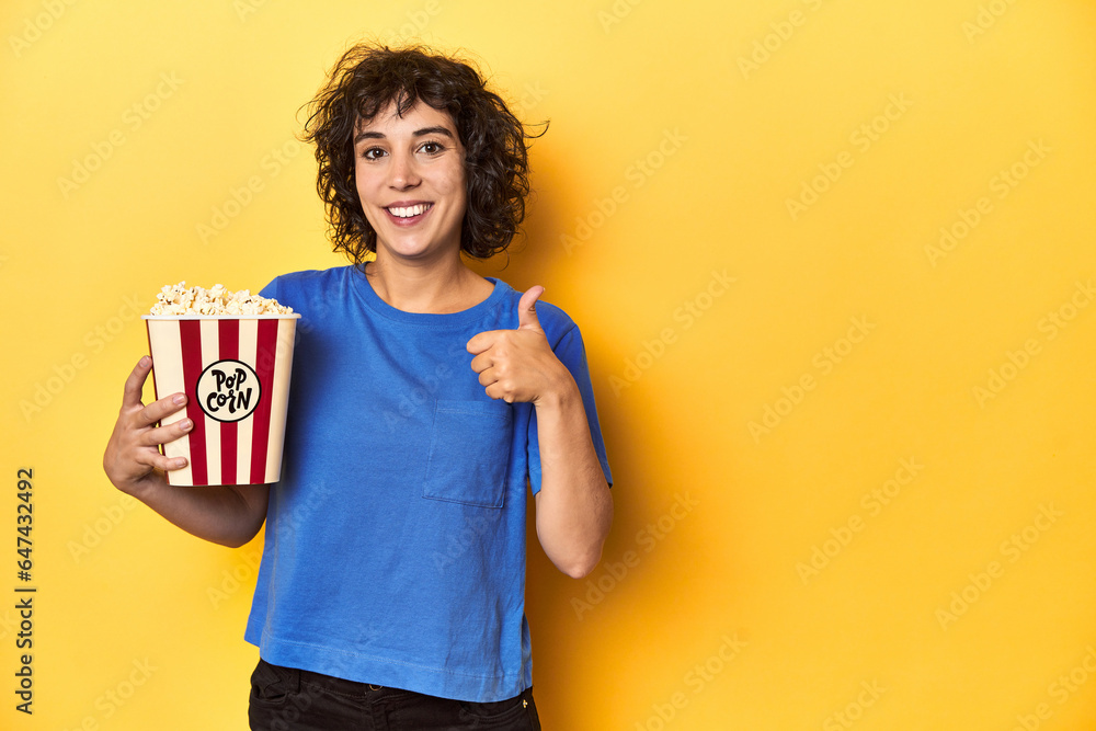 Curly-haired woman with popcorn for movie, studio smiling and raising thumb up Curly-haired woman with popcorn for movie, studio smiling and raising thumb up