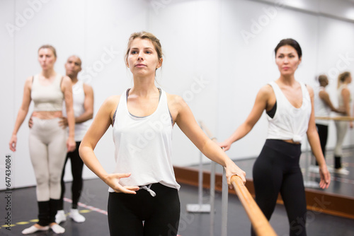 Group of people doing ballet exercises using barre in gym with focus to fit athletic toned woman in foreground in health and fitness concept