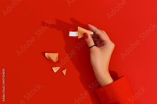 Women hands with manicure holding fortune cookie on red background. Blank paper for prediction words