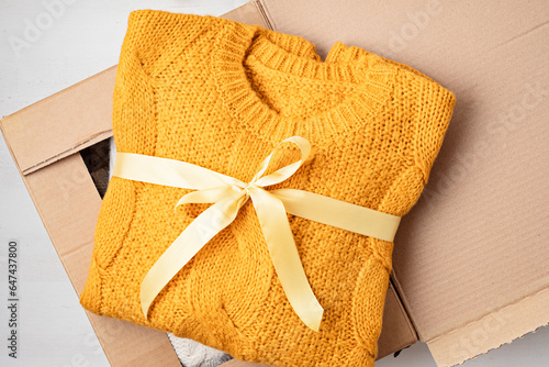 Unpaking delivery box with warm orange sweater inside. Online shopping, gifts for fall and winter seasonal holidays, christmas photo