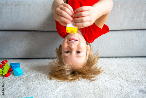 Smart looking caucasian child boy lying upside down on sofa, hanging his head down, smiling with joy and fun.