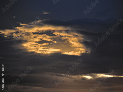 shaded clouds forming a window backlit by the twilight sun. © conpuli