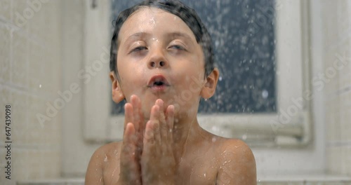Happy child enjoying bath time with droplets falling in super 800 fps slow-motion, young boy beaming with joy observing water flow standing in shower