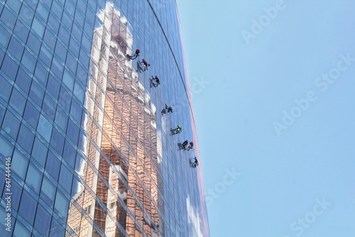 Team of professional climber workers cleaning outdoor windows of residential skyscraper. Industrial alpinism mountaineers washing outside at heights the glass facade of modern office building.