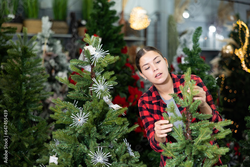 Smiling casual woman checking the material while standing near a Christmas tree in a shopping mall
