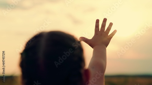 Hand of little girl at sunset. Sun between hands of kid girl. Happy child dreams stretches out his hand to sunset, summer park. Child dream hand to sun. Happy family on walk. Childs prayer outdoors