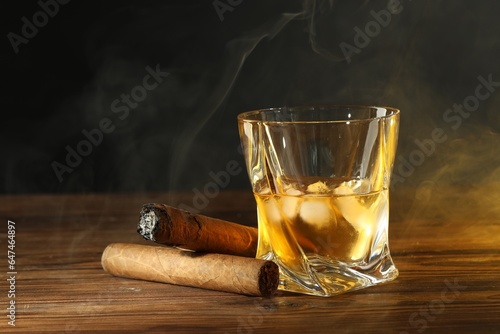 Glass of whiskey with ice cubes and cigars on wooden table