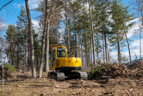 Obraz na płótnie Yellow excavator or digger machine, seen from behind, is clearing trees in preparation for the building of a new home on a construction site. w salonie