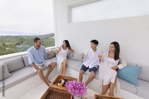 Summer meeting of friends in luxury terrace of tropiccal hotel, two men and two women sitting on sofa, relax time concept, copy space photo