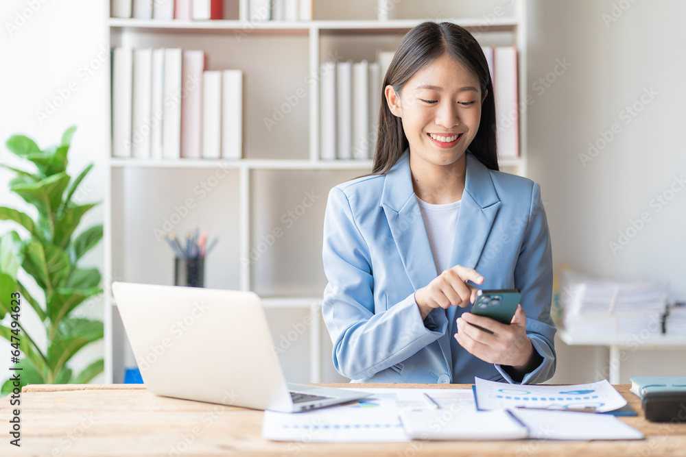 Happy young Asian business woman working with financial documents and laptop and smartphone