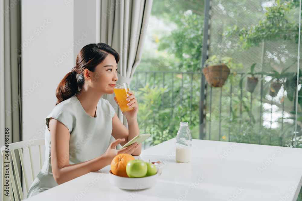Beautiful woman drinking orange juice and reading the news online in the kitchen Beautiful woman drinking orange juice and reading the news online in the kitchen
