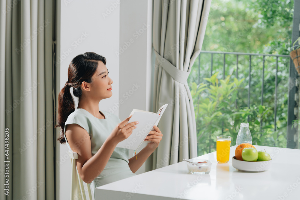 woman reading book in kitchen near fresh apples and orange juice on table