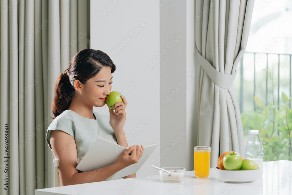happy woman reading book while having breakfast by table at home happy woman reading book while having breakfast by table at home