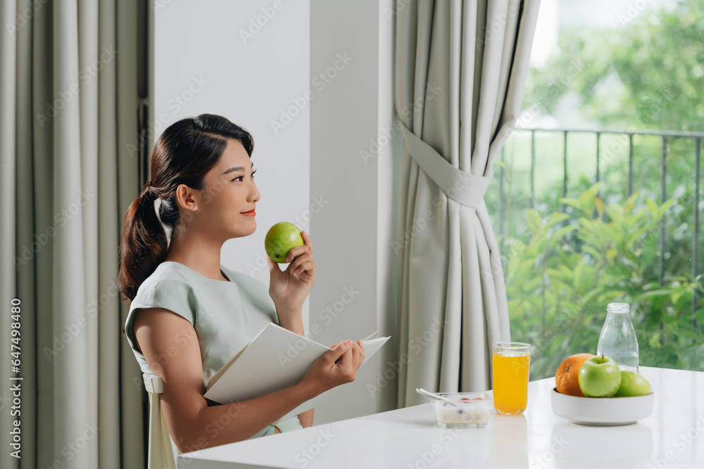A happy young woman sitting indoors at living room holding book reading drinking orange juice. A happy young woman sitting indoors at living room holding book reading drinking orange juice.