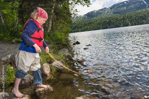 Young Girl With Bare Feet Wearing A Red Bandana And Lifejacket Playing With A Homemade Toy Wood Raft On A String At Byers Lake, Denali State Park; Alaska, United States Of America photo