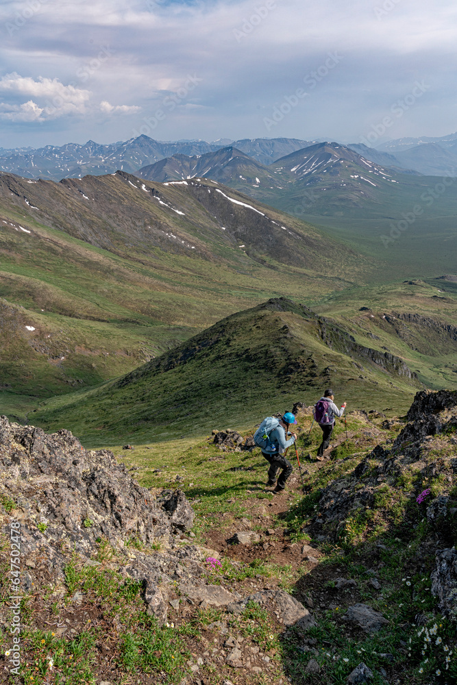 Two women hiking down a mountain side in Northern Yukon with beautiful views all around them along the Dempster Highway; Yukon Territory, Canada Two women hiking down a mountain side in Northern Yukon with beautiful views all around them along the Dempster Highway; Yukon Territory, Canada