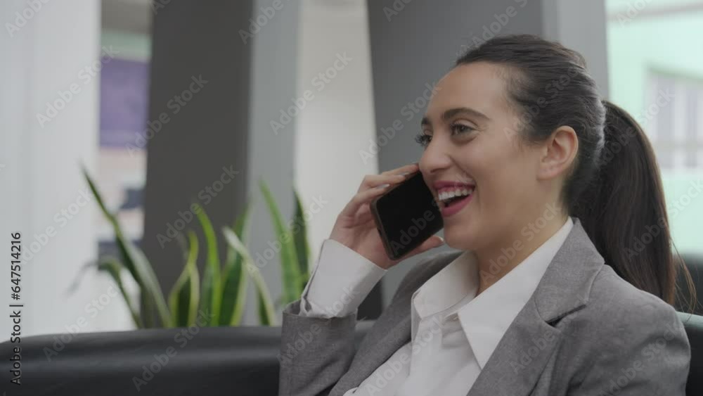 A young businesswoman, sitting in an armchair, has a conversation with a client on a cell phone, laughing loudly. Medium close-up, slow motion. A young businesswoman, sitting in an armchair, has a conversation with a client on a cell phone, laughing loudly. Medium close-up, slow motion.
