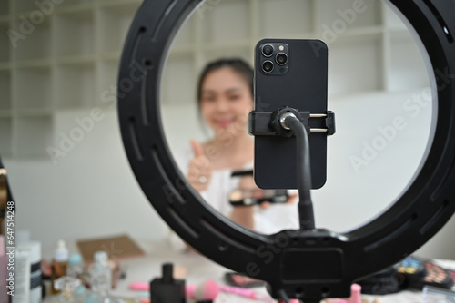 Female beauty blogger recording video and communicating with social media using mobile phone and ring lamp at home