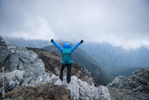 Woman hiker enjoy the view on mountain top cliff edge face the snow capped mountains in tibet