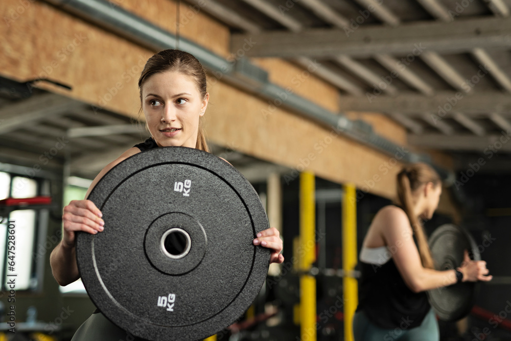 Fit young woman at a crossfit style on gym with barbell disk. Fitness, functional, training, and lifestyle concept. Indoors. Healthy lifestyle, lifting and body care. Fit young woman at a crossfit style on gym with barbell disk. Fitness, functional, training, and lifestyle concept. Indoors. Healthy lifestyle, lifting and body care.
