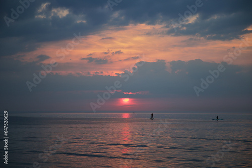 Sunset above the sea with small figures of people sailing on supboards, selective focus photo