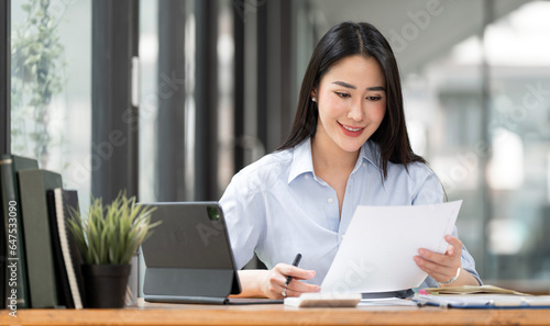 Cheerful business woman working on laptop in office, Asian happy beautiful businesswoman in formal suit work in workplace. Attractive female employee office worker smile.