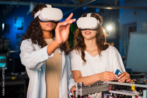 Obraz na płótnie Two young women in VR glasses doing experiments in robotics in a laboratory w salonie