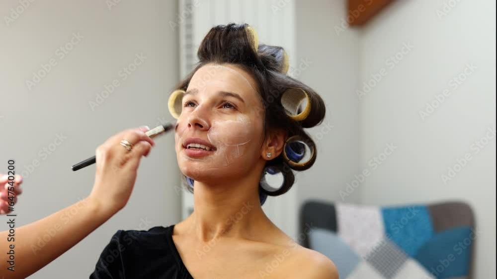 make up artist applying powder,cream, foundation, painting eyebrows, lips,putting false eyelashes.woman with curlers on hair. smiling female different angles.getting ready in beauty salon,4k video