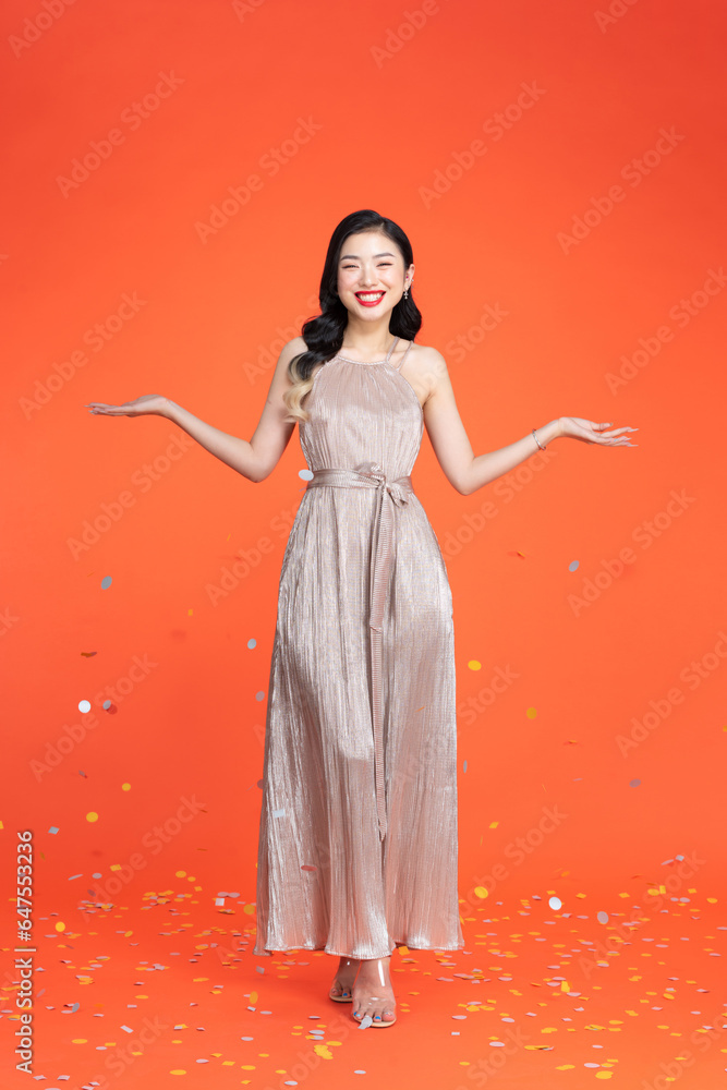 Portrait of a smiling beautiful woman in shiny dress having a party while standing under confetti rain Portrait of a smiling beautiful woman in shiny dress having a party while standing under confetti rain