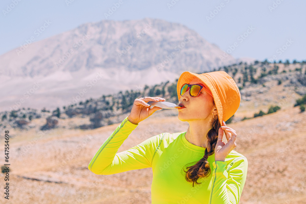 Pretty young woman biting on a energy sportive gel drink after a good hike in high mountains