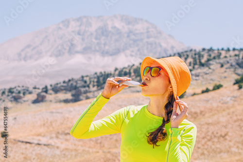 Pretty young woman biting on a energy sportive gel drink after a good hike in high mountains