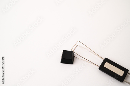 A close-up of a detached mechanical keyboard keycap placed near a stainless steal keycap and switch puller tool on a white background. Copy space.