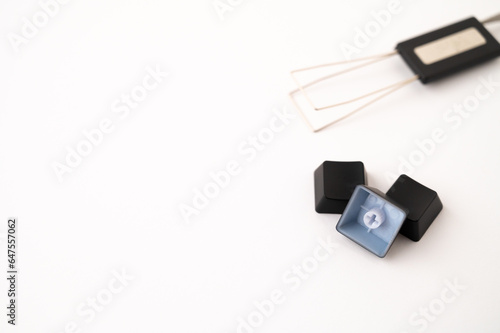 A close-up of a pile of three detached mechanical keyboard keycaps placed near a stainless steal keycap and switch puller tool on a white background. Copy space.