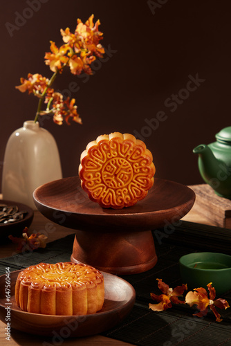 Delicious Chinese traditional mooncakes displayed on wooden dishes. Green tea set arranged behind with a flower pot. A time of year that the moon is at its brightest