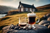 Nahaufnahme eines dampfenden Glases Irish Coffee neben einer Whiskeyflasche im Freien auf einem Felsen mit irischer Landschaft im Hintergrund.