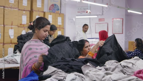 A group of Indian Asian women or female workers in traditional or ethnic wear checking or examining the ready outfits or dresses in a textile workshop or a small scale garment industry 