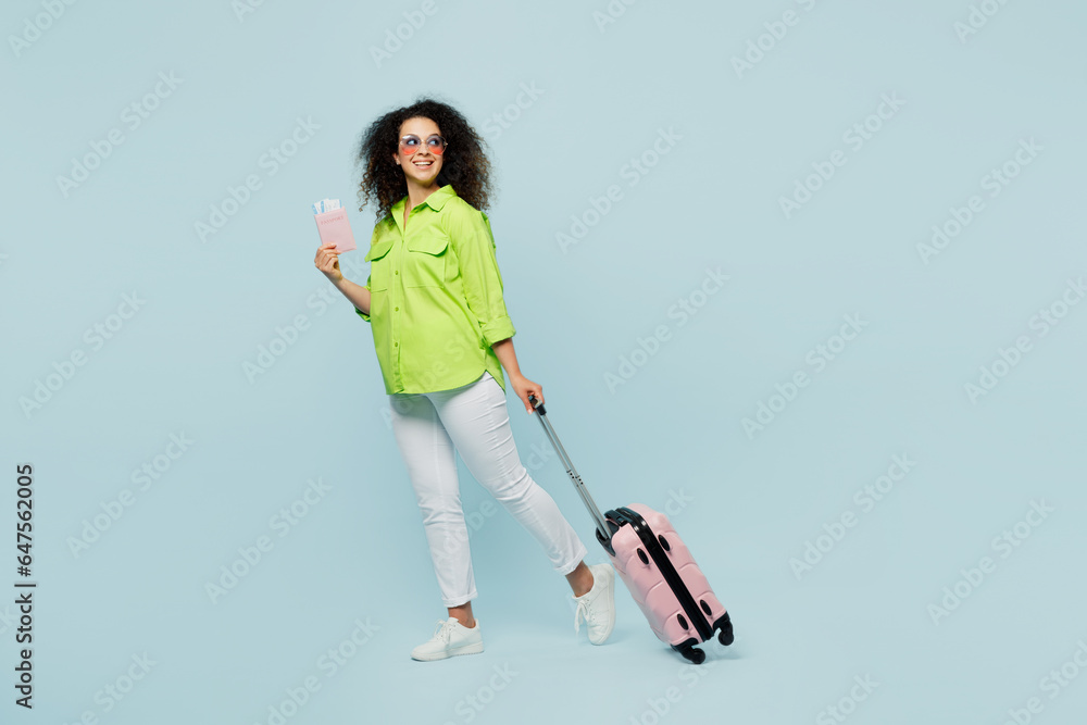 Traveler latin woman wear green casual clothes hold bag passport ticket look aside isolated on plain blue background. Tourist travel abroad in free time rest getaway. Air flight trip journey concept.