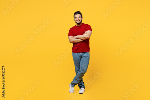 Full body young smiling cheerful cool happy Indian man he wears red t-shirt casual clothes hold hands crossed folded look camera isolated on plain yellow orange background studio. Lifestyle concept.