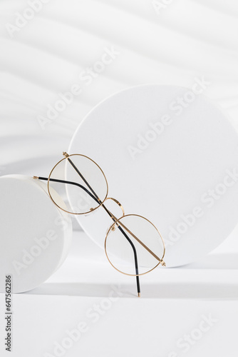 Unisex eyeglasses in a golden metallic frame on podium on white background. Vertical, close up. The product minimal still life. Optic store discount, sale. Copy space. Trendy eyewear photography