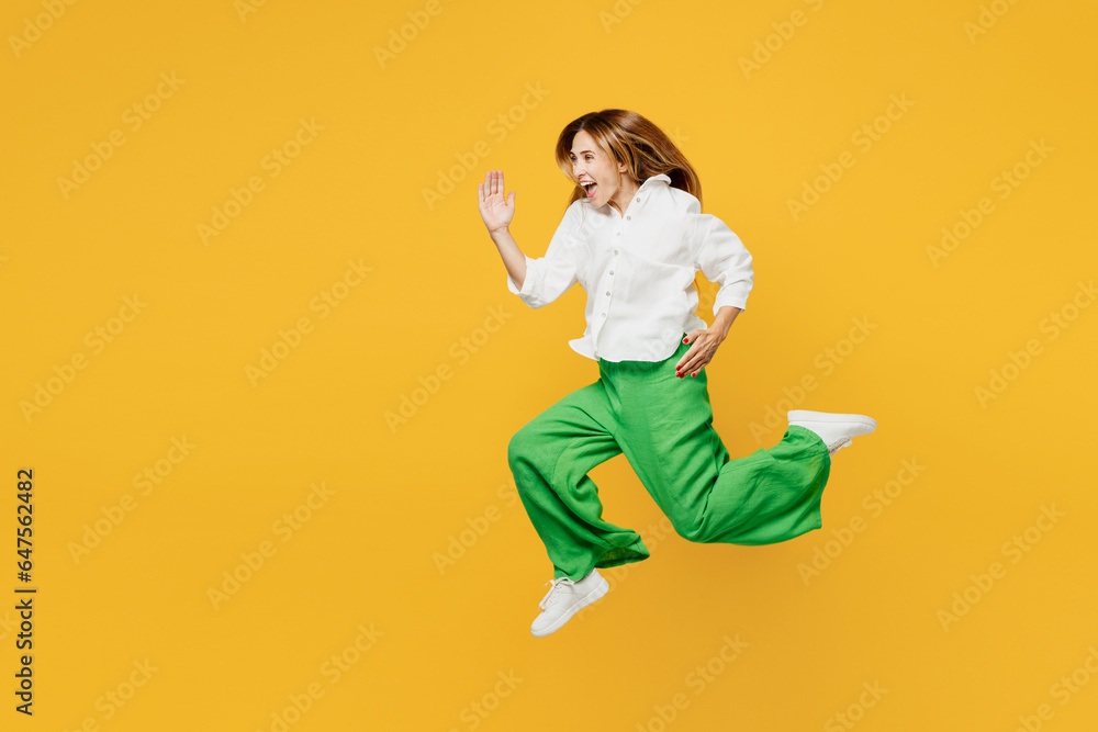 Full body side profile view young excited caucasian happy woman she wears white shirt casual clothes jump high run fast hurry up isolated on plain yellow background studio portrait. Lifestyle concept.